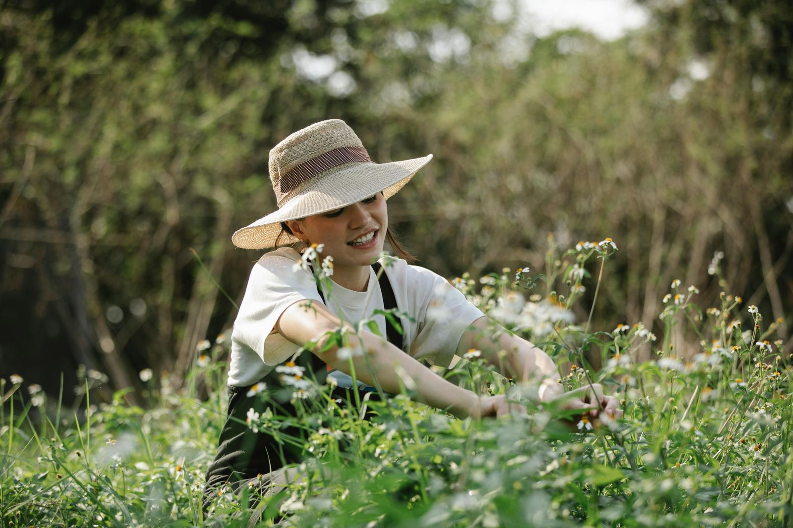 Woman in a wide brim straw hat tending wildflowers outdoors — sun protection as a way of living