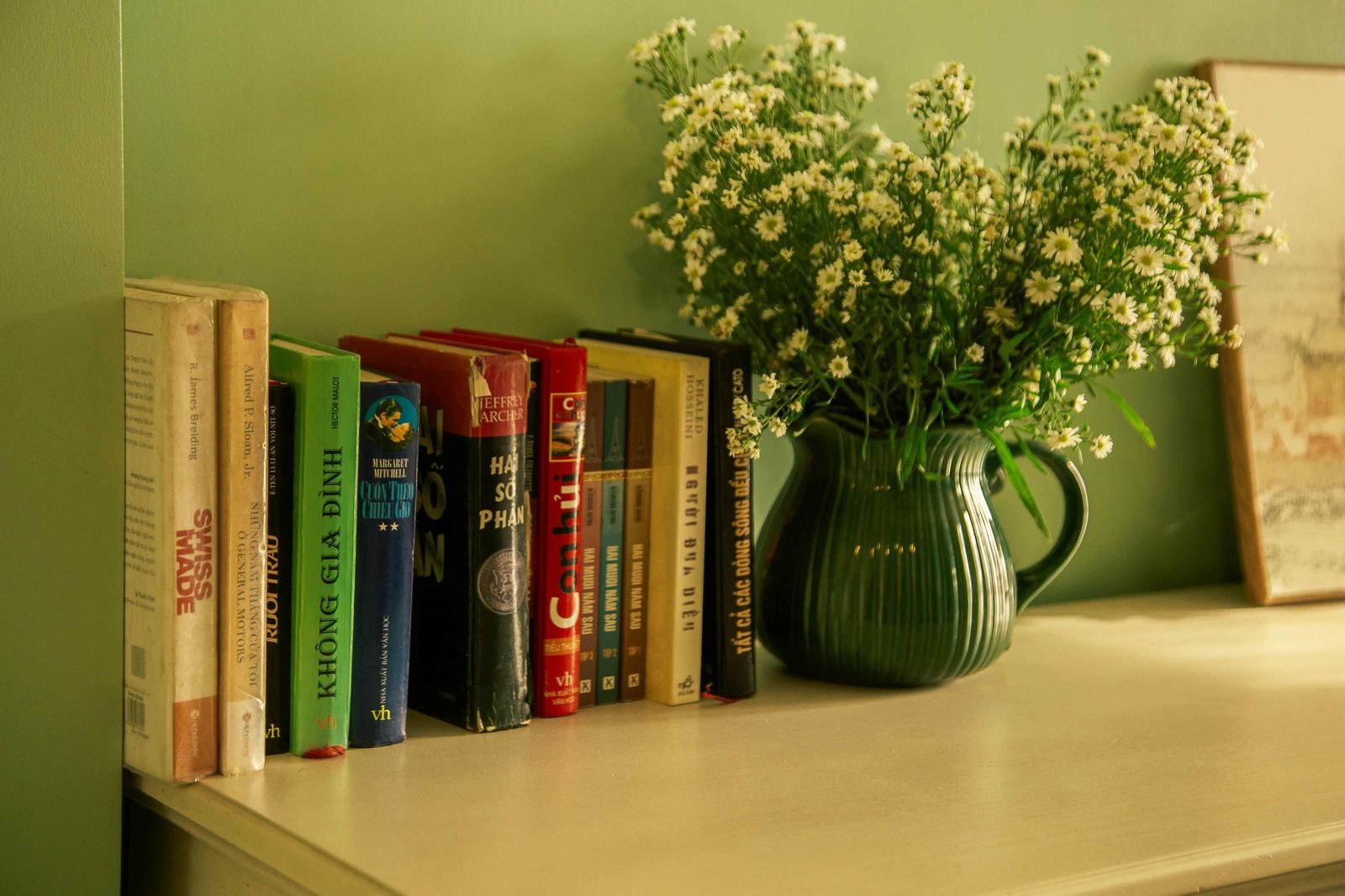 Books lined on a shelf beside a green vase of white wildflowers — a personal corner made intentional