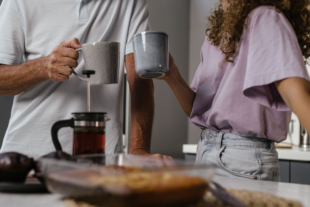 One partner pouring coffee and handing a mug to the other in the kitchen