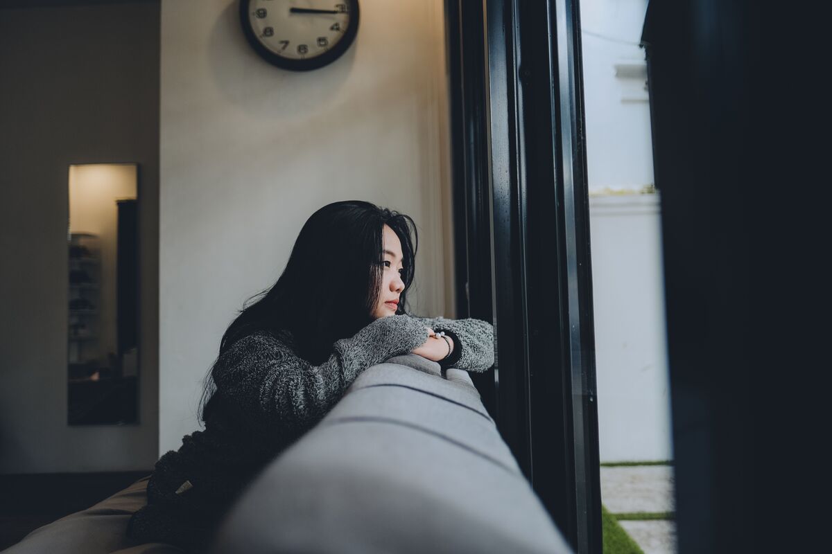A woman sitting quietly by a window in soft light, thoughtful and still