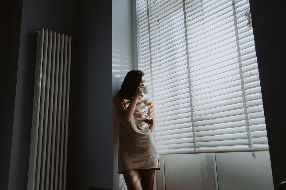 A woman sitting alone in quiet morning light, holding a cup, thoughtful