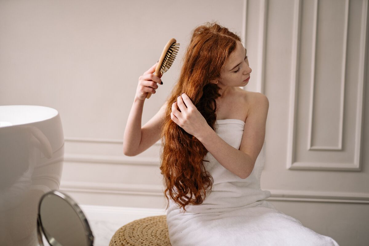 A woman gently detangling damp hair with a wide-tooth comb