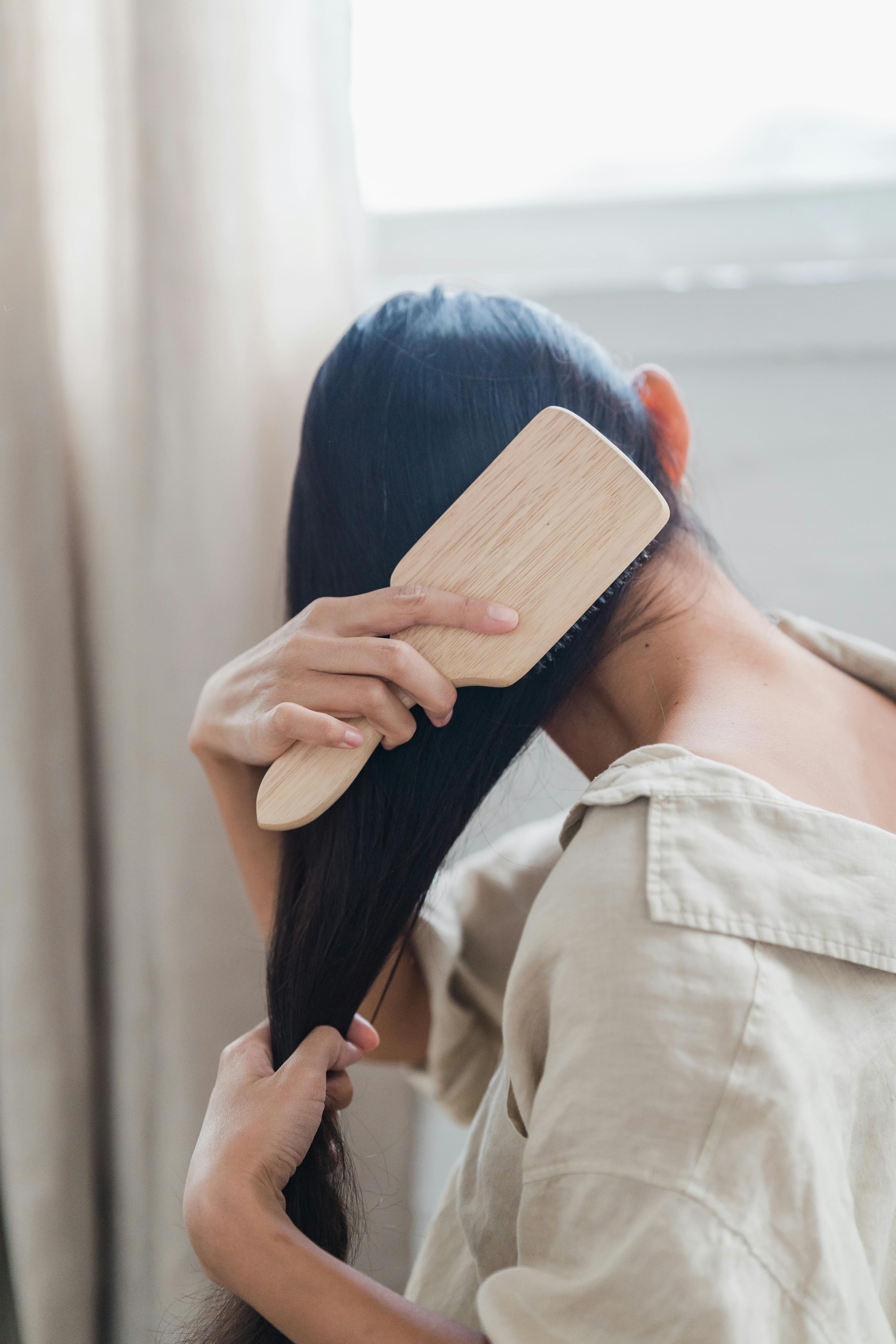 A woman brushing her long dark hair with a wooden brush in soft morning light