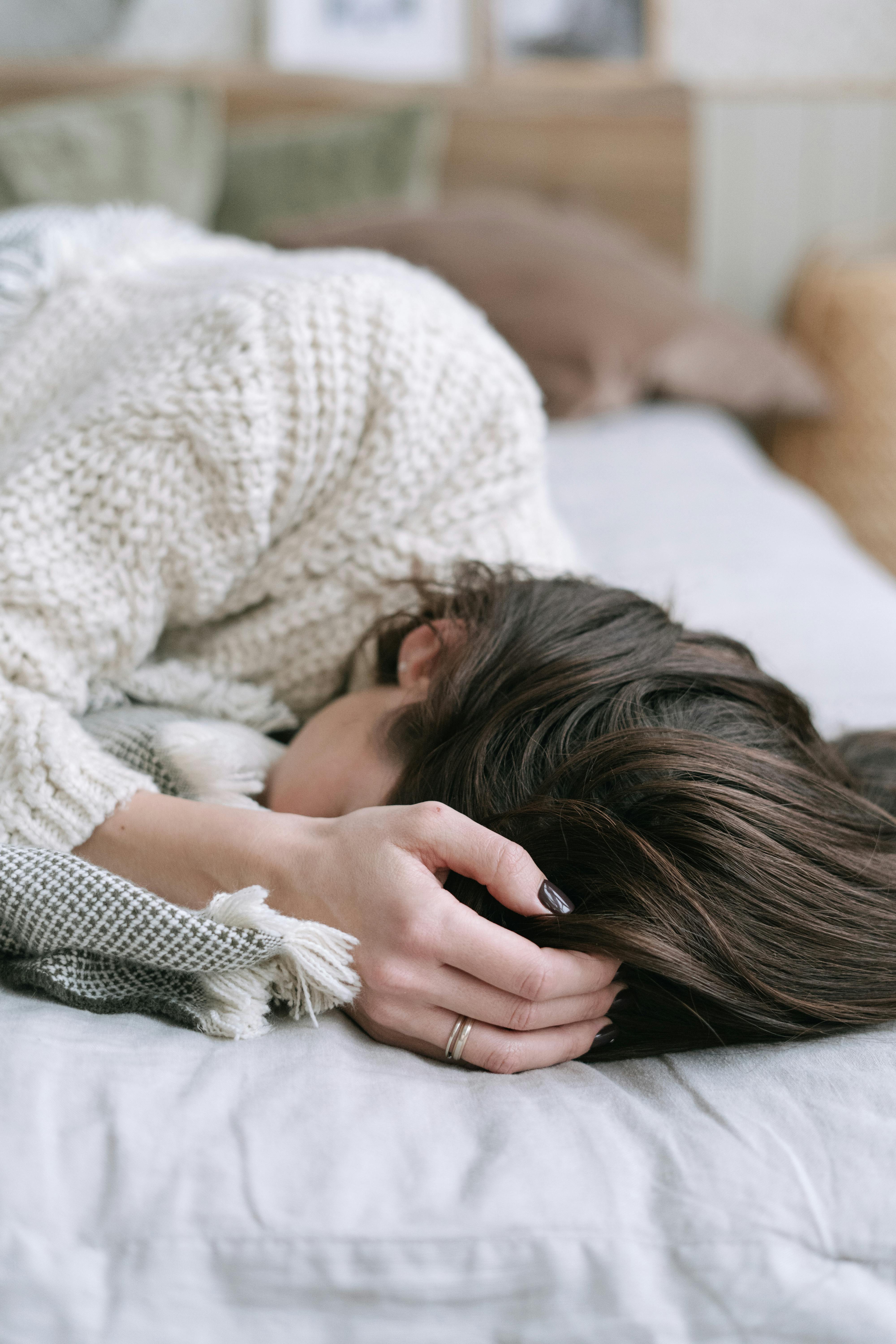A woman lying face-down on a bed in a knit sweater, quietly exhausted