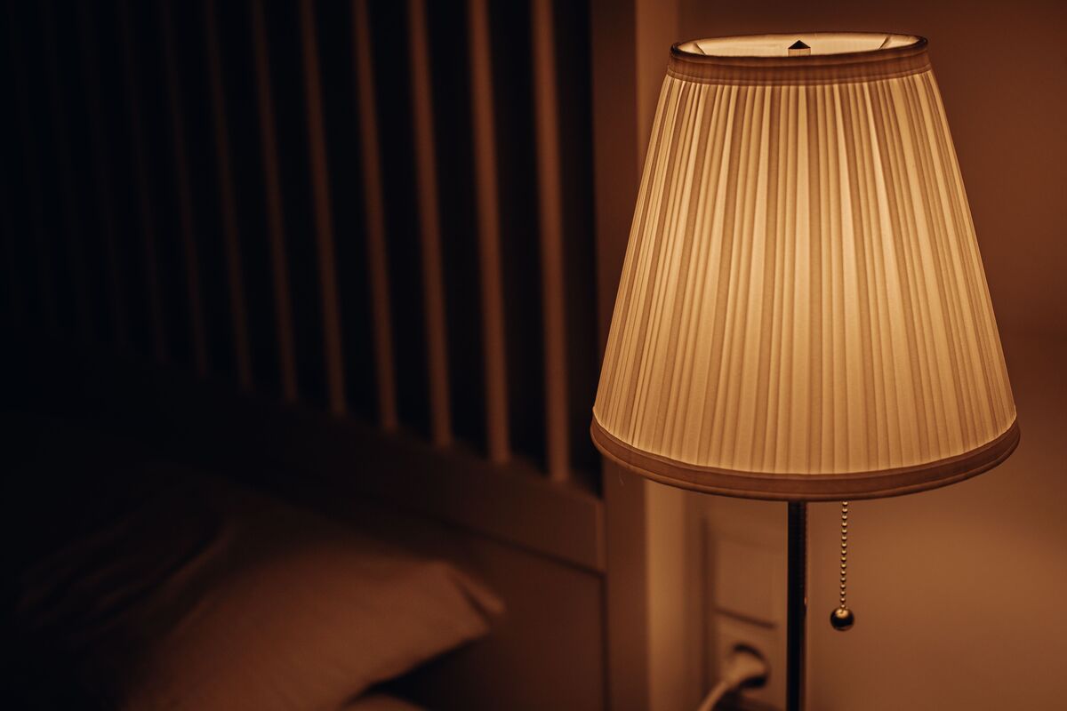 A dimly lit bedroom with a low warm lamp and a book on the bedside table