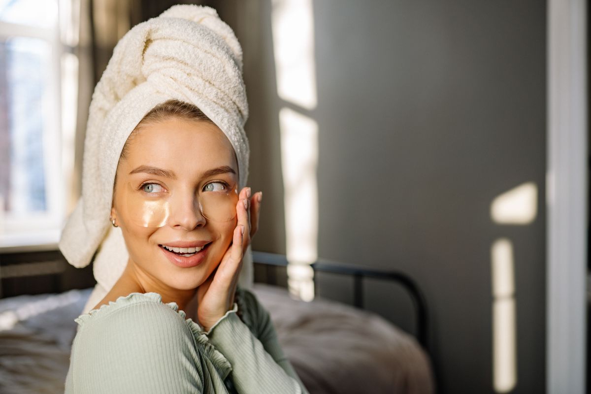 A woman applying skincare gently around her eye area in natural light